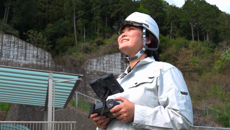 ドローンの操縦機を持ち空を見上げる女性社員